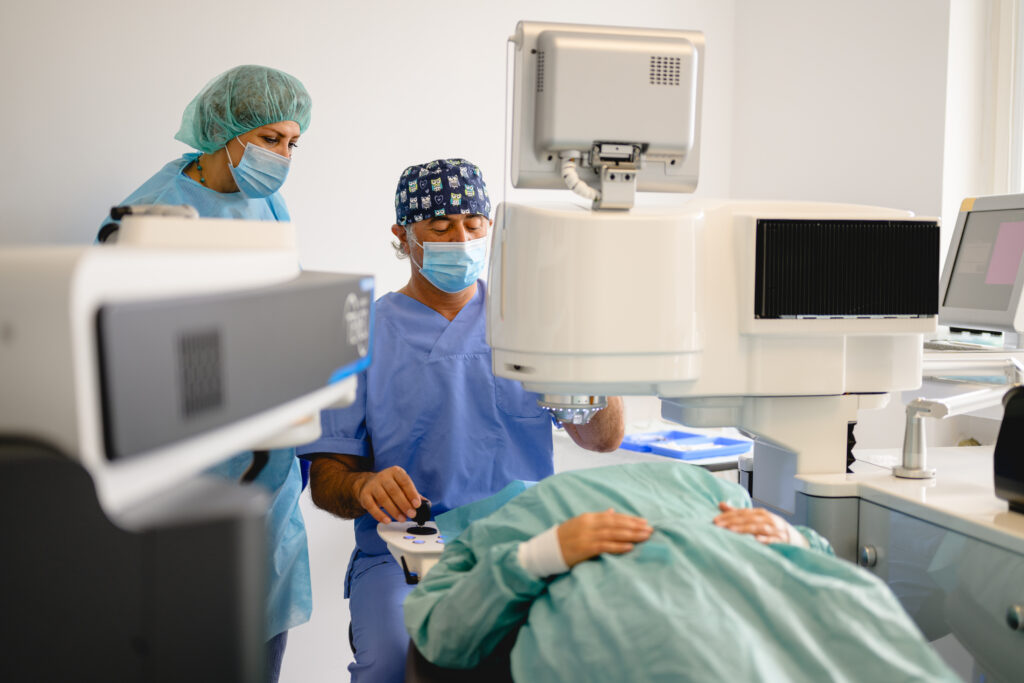 Zwei Mediziner in blauen Kitteln führen Laser-Augenoperation durch; Eine justierte Einstellungen, während der andere beobachtet.