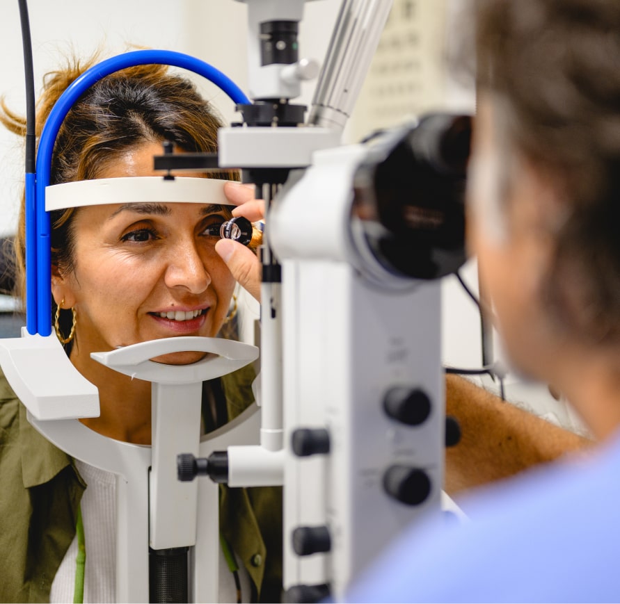 Frau unterzieht sich einer Augenuntersuchung an der Spaltlampe, untersucht vom Optiker. Das Auge wird für die Untersuchung beleuchtet.