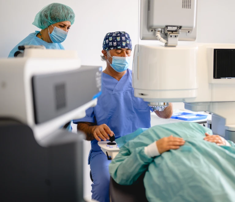 Mediziner führen Augenoperation mit Laser durch, Patient auf OP-Tisch; Alle tragen Schutzkleidung und Masken.