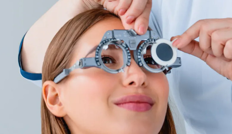 Eine Person wird mit einem Phoropter untersucht, während ein Optometrist die Linsen einstellt, um die Sehkraft zu testen.