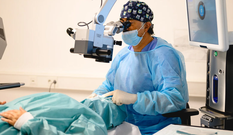 Ein Chirurg in blauem Kittel operiert einen Patienten mit Mikroskop und moderner Ausrüstung im Operationssaal eines Krankenhauses.