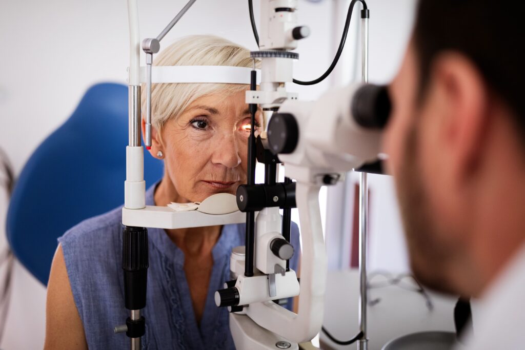 Eine ältere Frau schaut in ein Augenuntersuchungsgerät, während ein Optiker in einer Klinik ihre Sehkraft überprüft.