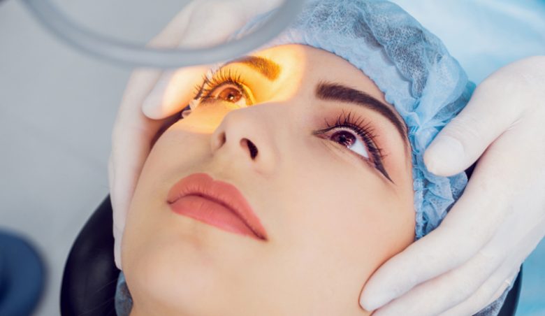 Person in blauer OP-Haube sitzt für Augenuntersuchung oder medizinisches Verfahren auf einem Untersuchungsstuhl unter hellem Licht.